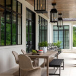 Covered patio with wood ceiling, black framed windows, wicker chairs, and dining table