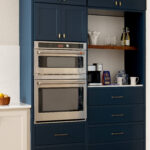 Navy blue kitchen cabinets with stainless steel double ovens and brass hardware