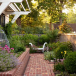 Brick pathway through a garden with a white bench and lush greenery.