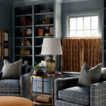Living room with blue plaid armchairs, built-in bookshelves, and a brass lamp.