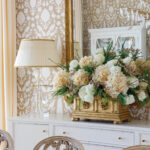 Dining room with white buffet, floral arrangement, crystal lamp, and patterned wallpaper