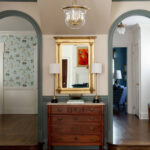 Hallway with arched doorways, wood dresser, gold mirror, and patterned wallpaper