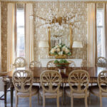 Dining room with ornate chairs, wood table, floral centerpiece, and gold chandelier.