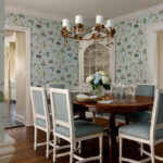 Dining room with bird and branch wallpaper, round wood table, and upholstered chairs