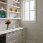 Pantry with white cabinetry, marble countertop, floral wallpaper, and a window.