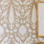 Tan wallpaper with white peacock and floral pattern. Gold picture frames on right.