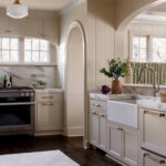 Cream kitchen with marble counters, apron sink, brass hardware, and paneled walls.
