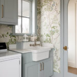 Laundry room with light blue cabinets, white farmhouse sink, and bird and floral wallpaper.