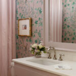 Pink bathroom vanity with white countertop and sink, floral wallpaper, and striped shower curtain.