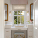 White bathroom vanity with gold fixtures and a pink window shade.