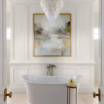White bathroom with freestanding tub, abstract art, and ornate chandelier
