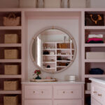 Pink closet with built-in shelves, round mirror, wicker baskets, and drawers.