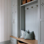 Mudroom with pale blue built-in cabinets, wood bench, and striped wallpaper.