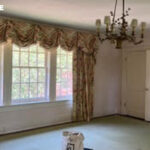 Room with floral curtains, green carpet, and a chandelier.