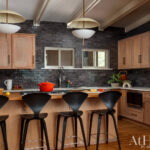 Kitchen with dark subway tile backsplash, wood cabinets, and black bar stools.