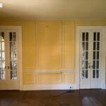 Yellow room with paneled walls, two sets of glass-paned double doors, and dark wood floor.