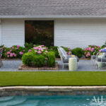 White brick house with pink hydrangeas, gravel patio, and outdoor seating by a pool
