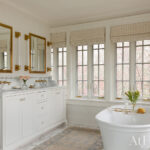 White bathroom with marble vanity, brass fixtures, and a freestanding tub.