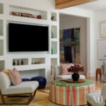 Living room with built-in shelves, textured chairs, striped ottoman, and artwork
