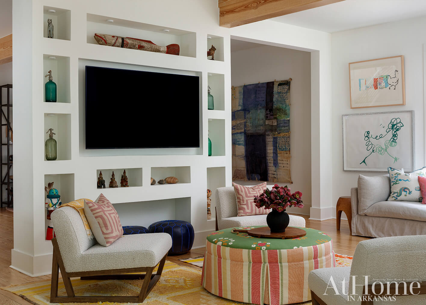 Living room with built-in shelves, textured chairs, striped ottoman, and artwork