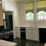 Kitchen with black gas range, white cabinets, white countertops, and three arched windows.