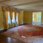 Living room with yellow walls, ornate gold curtains, and a large red Persian rug.