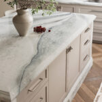Kitchen island with marble countertop, beige cabinetry, and brushed nickel hardware.