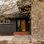 Mid-century modern home with stone and dark brick exterior, yellow door.