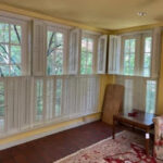 Sunroom with yellow walls, white plantation shutters, brick floor, and patterned rug.