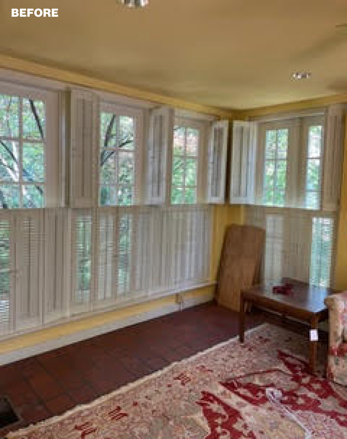 Sunroom with yellow walls, white plantation shutters, brick floor, and patterned rug.