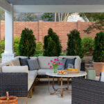 Covered patio with sectional sofa, marble table with tulips and pastries, and brick wall