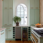 Mint green kitchen cabinets with brass hardware, marble countertops, and a gas range.