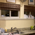 Kitchen sink with granite countertop, bamboo blinds, and framed art.