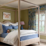 Bedroom with a four-poster bed, blue bedding, butterfly art, and floral curtains.