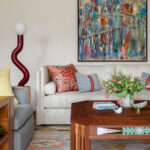Living room with neutral sofa, abstract bridge painting, and red sculptural lamp.