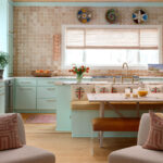 Mint green kitchen with tiled backsplash, built-in banquette, and wooden dining table.