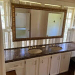 Bathroom vanity with double sinks, granite countertop, and white cabinets under a large ornate