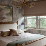 Bedroom with patterned wallpaper, quilted bed, and gold chandelier.