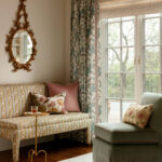Sofa with floral pattern, gold ornate mirror, and patterned curtains.