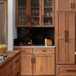 Kitchen with light wood cabinets, black subway tile backsplash, and glass-front upper cabinets.