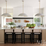 White kitchen with light wood island, marble counters, and pendant lights.