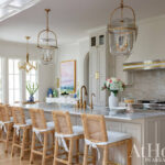 Cream kitchen with marble island, rattan bar stools, brass fixtures, and glass pendant lights