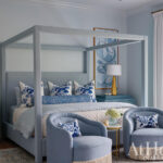 Blue bedroom with four-poster bed, upholstered chairs, and abstract art.
