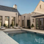 Luxury home with cream brick exterior, dark-framed windows, and pool.