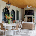 Covered patio with white dining set, wicker sofas, stone fireplace, and wood ceiling.