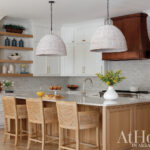 Kitchen with white cabinets, wood island, woven pendant lights, and cane bar stools.