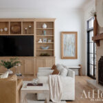Living room with light wood built-in entertainment center, stone fireplace, and neutral furniture.