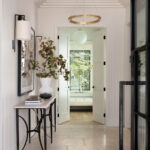 Hallway with fluted walls, stone tile floor, console table, and double doors leading to a sunroom.