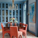 Dining room with blue built-in cabinets, coral velvet chairs, and abstract art