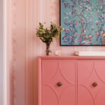 Pink cabinet with ornate hardware, floral artwork, and floral wallpaper